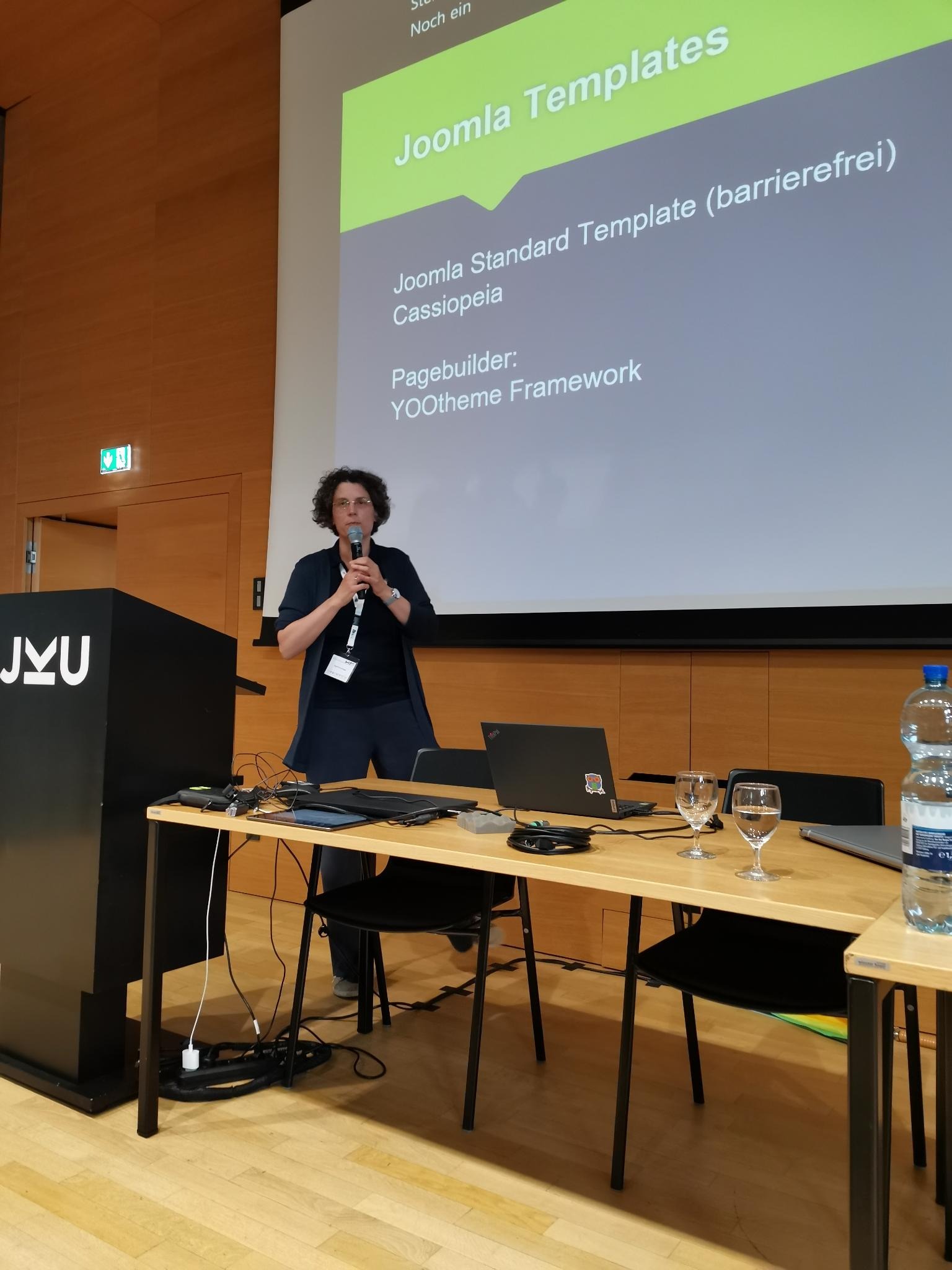 Sigrid Gramlinger steht vor einer Präsentationsleinwand zum Thema Barrierefreiheit mit Joomla mit einem Mikrofon in der Hand.