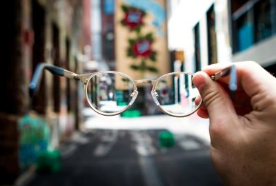 Jemand hält eine Brille vor einen unscharfen Hintergrund