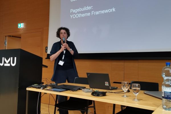 Sigrid Gramlinger steht vor einer Präsentationsleinwand zum Thema Barrierefreiheit mit Joomla mit einem Mikrofon in der Hand.