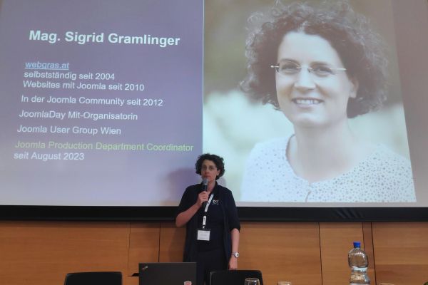 Sigrid Gramlinger steht vor einer Präsentationsleinwand zum Thema Barrierefreiheit mit Joomla mit einem Mikrofon in der Hand.